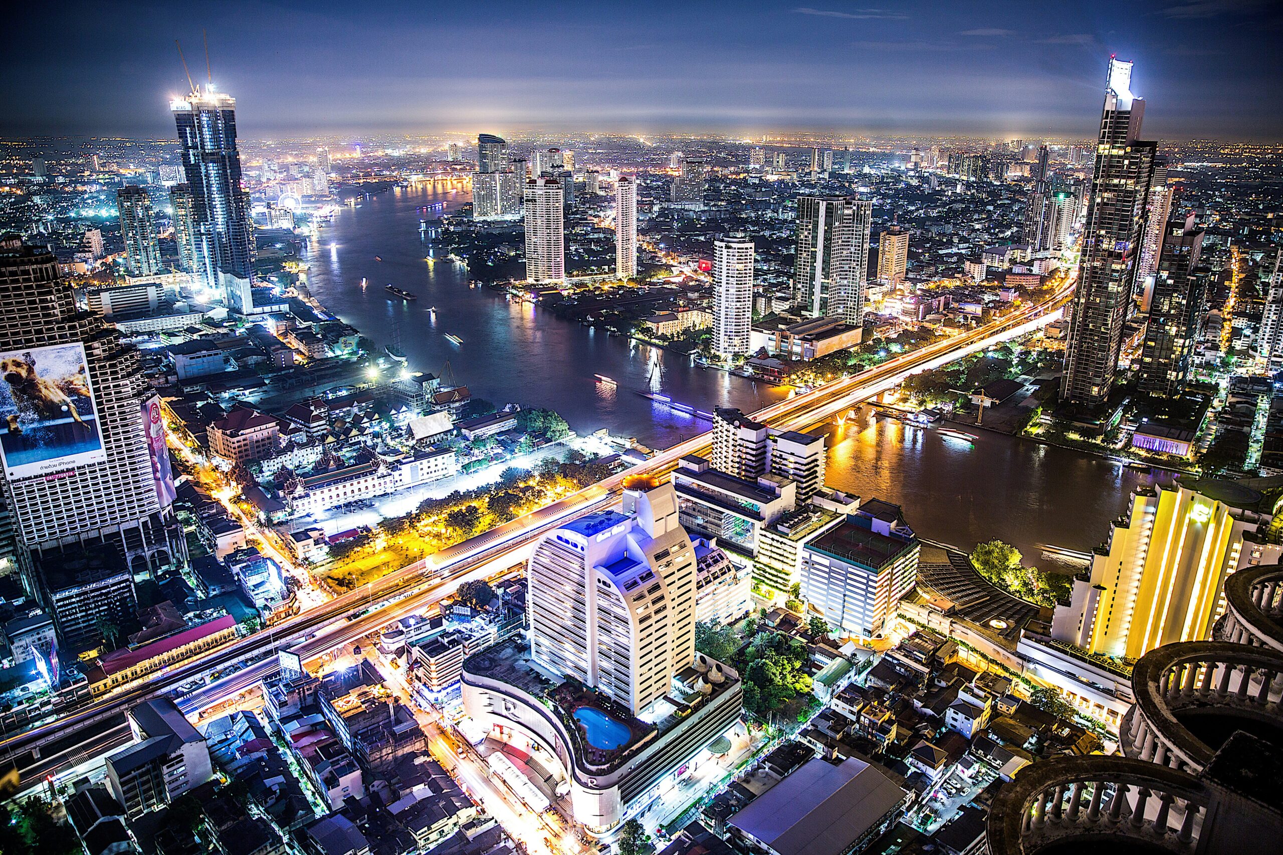 Vista aérea noturna de Bangkok, com arranha-céus iluminados e o rio Chao Phraya, cenário da terceira temporada de White Lotus na Tailândia.