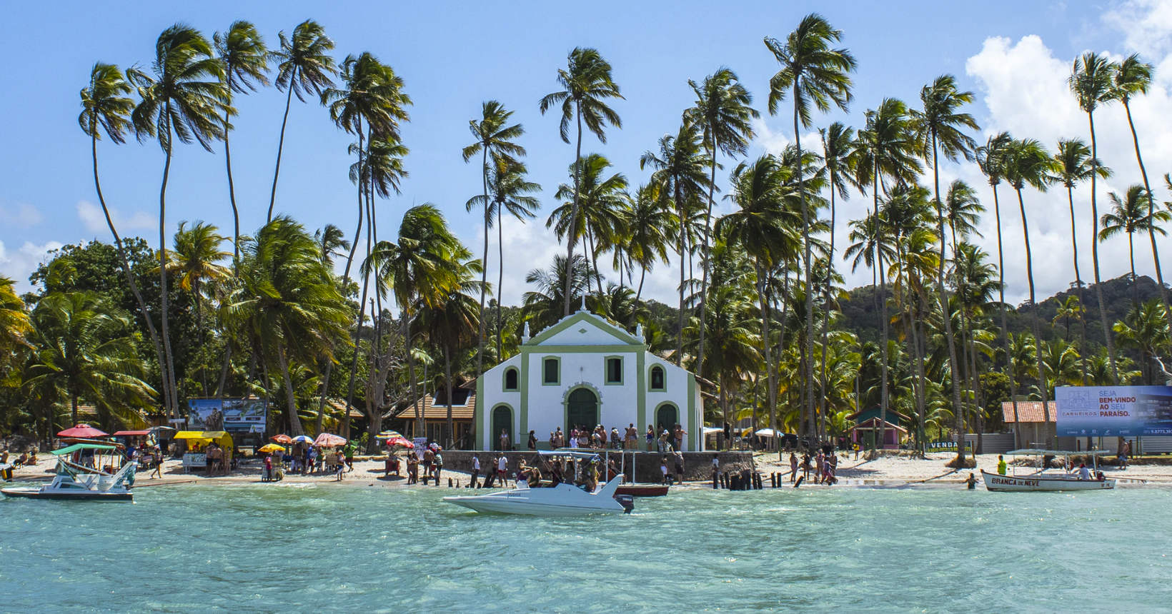 Capela de São Benedito cercada por coqueiros e águas cristalinas na Praia dos Carneiros, Pernambuco, cenário perfeito para o Réveillon 2025.