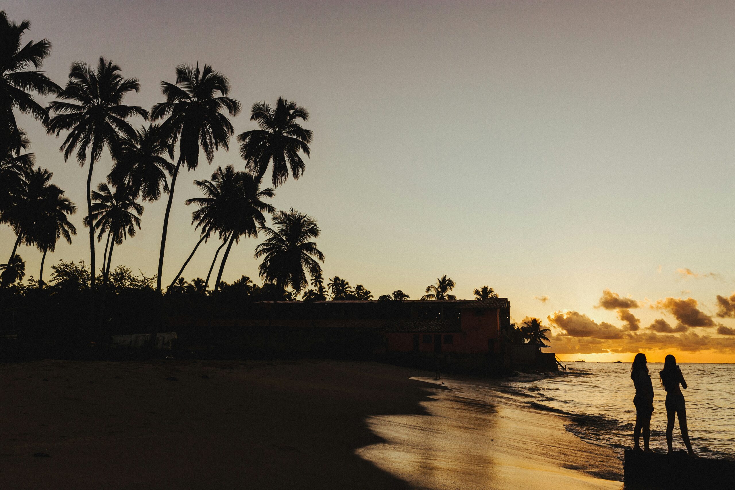 Silhueta de coqueiros e duas pessoas apreciando o pôr do sol em Maragogi, um dos vencedores do Prêmio O Melhor de Viagem e Turismo 2024/2025.