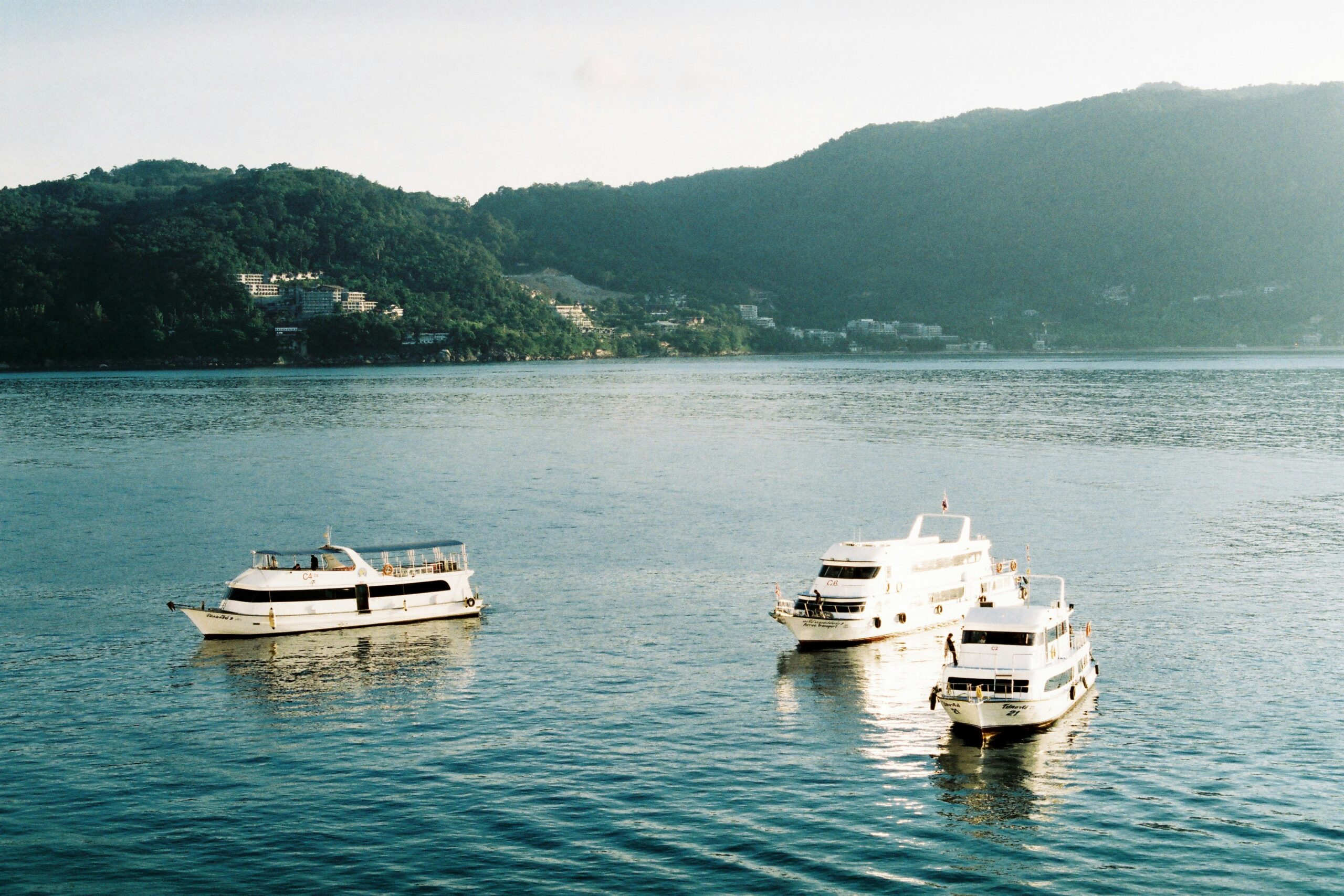 Barcos ancorados em águas tranquilas com montanhas ao fundo em Phuket, Tailândia, cenário da terceira temporada de White Lotus na HBO MAX.