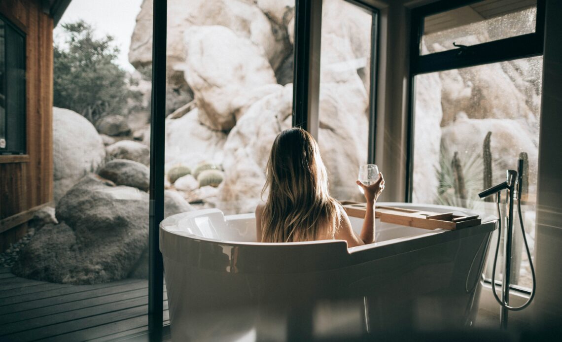 Mulher relaxando em uma banheira em um SPA em Búzios, com vista para pedras e natureza.