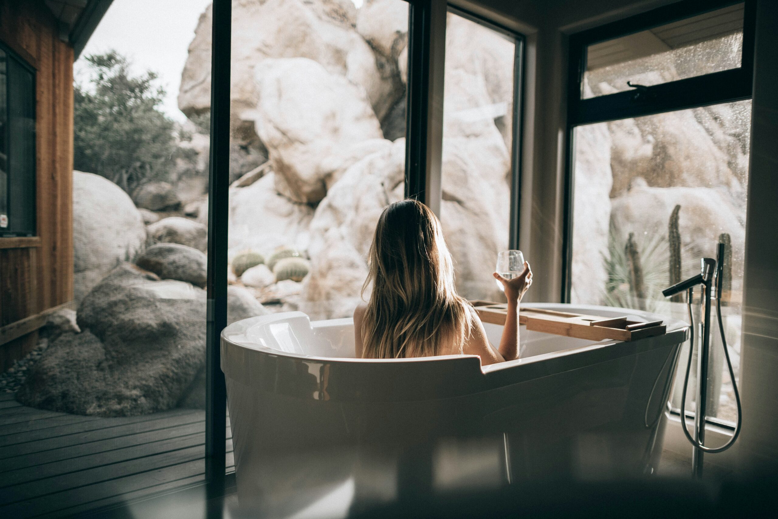 Mulher relaxando em uma banheira em um SPA em Búzios, com vista para pedras e natureza.