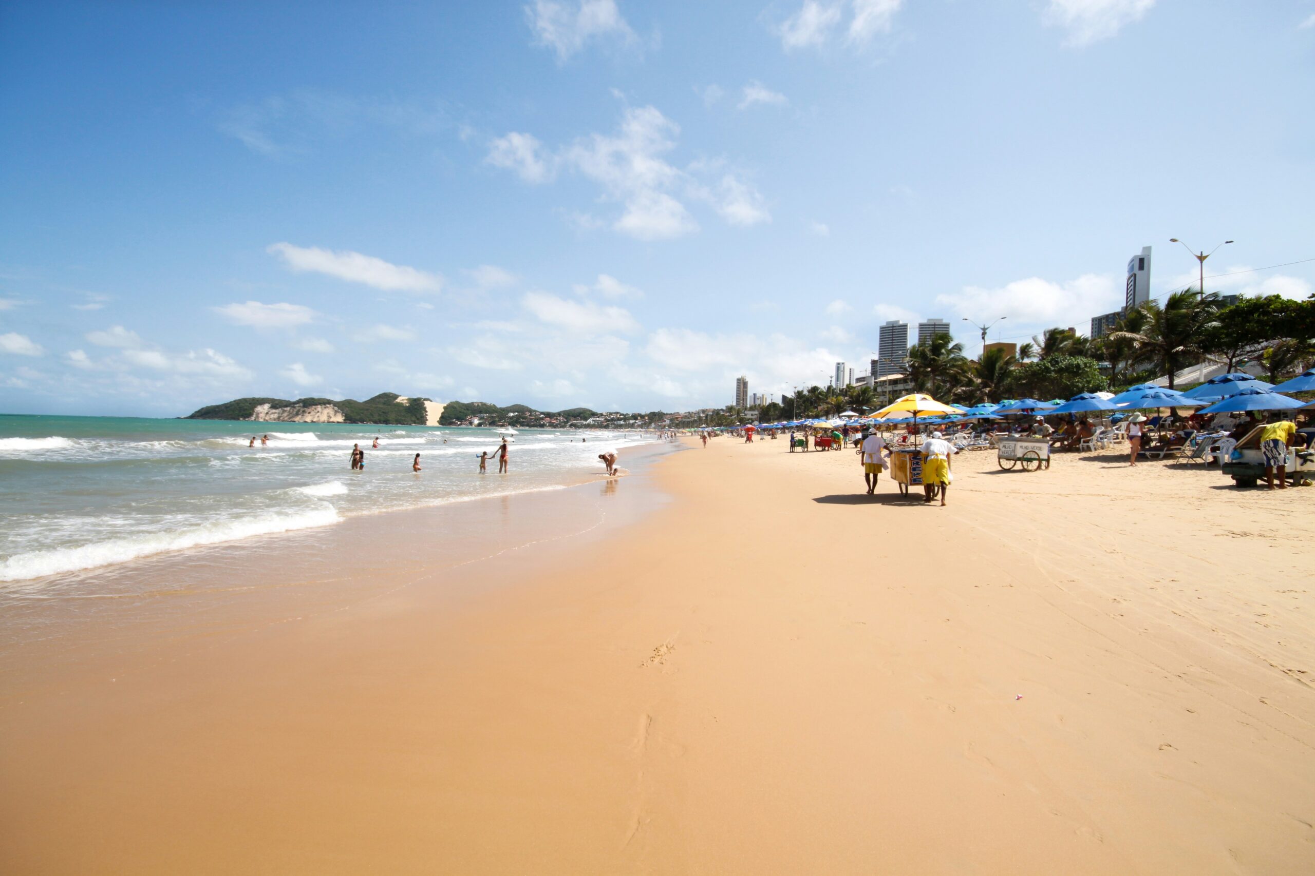 Vista da Praia de Ponta Negra em Natal (RN), com areia dourada, mar tranquilo e o icônico Morro do Careca ao fundo.