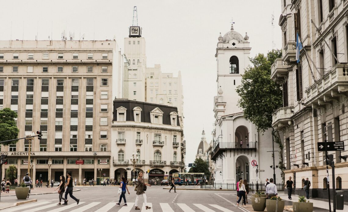 Cruzamento em Buenos Aires com arquitetura histórica e pedestres atravessando, refletindo o impacto econômico no turismo da Argentina.